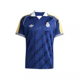 Camiseta de fútbol Adidas Originals del Real Madrid, color azul oscuro con estampado jacquard de logotipos. Presenta cuello polo blanco, mangas con las icónicas tres tiras en amarillo y detalles en blanco y azul en los puños.