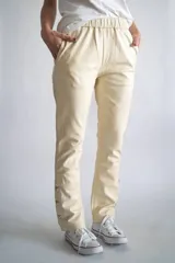 Pantalón de cuero color beige, con cintura elástica, bolsillos laterales y detalle de botones metálicos en los tobillos.