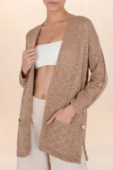 Cardigan largo marrón de tejido ligero, con diseño abierto y holgado, bolsillos frontales y botones decorativos en los costados.