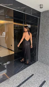 Vestido largo negro con escote halter cruzado y abertura frontal. El ruedo presenta un detalle de flecos.