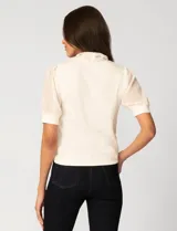 Blusa de color blanco con escote en V y detalle de lazo frontal. Presenta mangas cortas de gasa con terminación en puño.