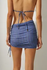 Falda corta tipo pareo con diseño de rayas verticales en tonos azul y negro. Presenta un lateral fruncido con cordón ajustable que permite regular el largo y el ajuste de la prenda.