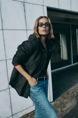 Chaqueta acolchada de color negro con diseño de costuras onduladas, cuello subido y capucha ajustable. Cuenta con cierre frontal de cremallera oculto por una solapa con botones a presión, mangas largas y bolsillos laterales. Tejido con tecnología repelente al agua.