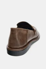 Mocasín de cuero color marrón con diseño de antifaz en el empeine, acabado en punta redonda y suela plana con efecto desgastado.