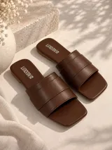 Sandalias planas de cuero sintético color marrón, con diseño de tiras anchas acolchadas y punta cuadrada.