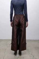 Pantalón de tafeta tornasolada color borgoña, de corte recto y tiro alto, con cintura elastizada, bolsillos frontales con cierre y cordones ajustables en las pantorrillas para fruncir el bajo.