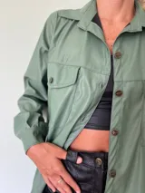 Camisa verde de cuero sintético con cuello clásico, cierre frontal con botones metálicos y dos bolsillos con solapa en el pecho.