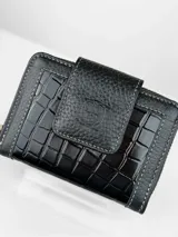 Billetera compacta de cuero negro con diseño combinado de textura granulada y efecto crocco brillante. Cuenta con cierre perimetral, solapa frontal con broche y logo grabado, e incluye una correa de muñeca extraíble.