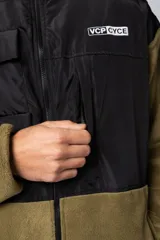 Campera de polar con recortes en tela técnica tipo sire en la parte superior frontal. Presenta cierre frontal completo, cuello alto y bolsillos funcionales en el pecho. Diseño bicolor en tonos verde oliva y negro con logo de la marca en el pecho.