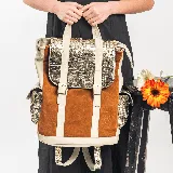 Mochila de cuero vacuno color whisky, con detalles en dorado y manteca. Tiene un bolsillo con broche a presión a cada costado, y un bolsillo con cierre en la parte trasera. Posee cierre superior y una tapa con broche a presión. El interior está forrado en tela y contiene un bolsillo con cierre y otro pequeño para el móvil.