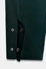 Pantalón de tiro alto color verde oscuro, confeccionado en mezcla de algodón. Presenta bolsillos laterales, detalle de tejido con volumen y costuras torcidas. Cierre frontal con cremallera, botón interior y ganchos metálicos ocultos.