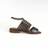 Sandalia plana color peltre, con tiras de cuero entretejidas en el empeine y pulsera con hebilla al tobillo.