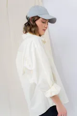 Camisa verde pastel de algodón, corte oversize, con cuello camisero, cierre con botones, mangas largas con puños con volados de encaje blanco, dos bolsillos frontales con solapa y ruedo irregular. 