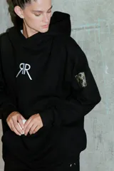 Buzo negro oversize de frisa con capucha amplia, bolsillo canguro, terminaciones de puño y ruedo con rib, y logo bordado en el centro delantero.