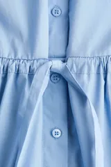 Vestido camisero corto de popelina de algodón en color celeste, con cuello clásico, cierre frontal con botones, mangas largas con puños sencillos y cordón ajustable en la cintura.