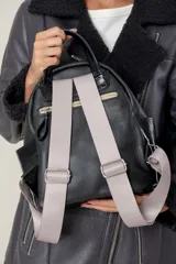 Mochila de cuero gamuzado color marrón con detalles en cuero metalizado plateado. Cuenta con cierre frontal, correas de cinta ajustables y placa metálica con logo de la marca en la parte inferior.