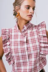 Blusa sin mangas color blanco con cuello alto con volados y detalles de volados en los hombros. Cuenta con cierre frontal de botones.
