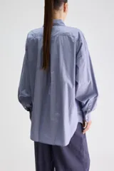 Camisa de silueta oversize de algodón color celeste, con cuello clásico, cierre frontal con botones, hombros caídos, bolsillo aplicado en el pecho y puños abotonados.