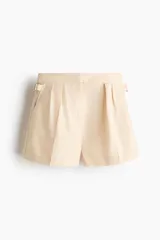 Short en tejido de mezcla de algodón y lino de color beige, con pinzas delanteras, bolsillos laterales al bies y trabillas ajustables con hebilla en los laterales de la cintura.