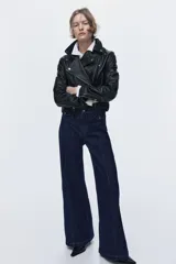 Pantalón de jean de denim azul oscuro, de tiro alto y piernas amplias con corte holgado. Presenta solapas de bolsillo decorativas con botón en el frente y costuras verticales visibles a lo largo de las piernas.