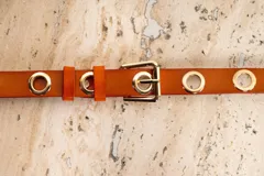 Cinto de cuero color whisky con hebilla metálica dorada y ojales metálicos dorados.