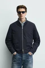 Sobrecamisa de corte regular fit en tejido técnico negro resistente al agua, con cuello estilo bomber en rib elástico, cierre frontal de cremallera y bolsillos plastrón con solapa en la cadera.