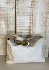 Cartera de hombro color beige con textura tipo cocodrilo, confeccionada en gamuza. Presenta un diseño estructurado con una cadena metálica decorativa en la parte superior del asa y cierre principal.