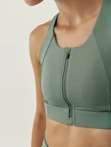 Top deportivo verde con cremallera frontal, de sujeción alta y tejido Shape_Tech con tecnología Performance.
