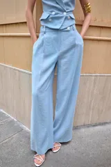 Pantalón celeste de tiro alto con pinzas delanteras, bolsillos laterales y falsos bolsillos traseros. Pierna ancha y cierre frontal con cremallera y botones.