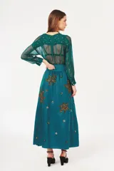 Falda larga color turquesa con cintura alta y apliques bordados de lentejuelas doradas y plateadas en forma de hojas o flores.