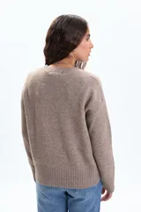 Buzo de tejido de punto en color beige, con cuello redondo a la base, mangas largas y puños y ruedo acanalados.