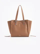Cartera tipo tote bag de cuero vacuno color marrón, con asas largas para el hombro y detalles de herrajes metálicos plateados en el frente.