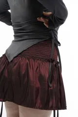 Top de manga larga color negro, confeccionado en jersey elástico. Presenta un diseño asimétrico con jaretas laterales regulables que permiten ajustar el largo y el volumen, y aberturas para los pulgares en los puños.