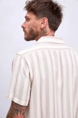 Camisa de manga corta color beige con rayas verticales marrones, cuello tipo cubano y bolsillo en el pecho.