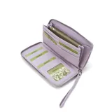 Billetera larga con cierre perimetral, confeccionada en material sintético texturizado color mostaza. Cuenta con correa de mano extraíble y placa metálica con logo de la marca en el frente.