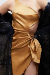 Vestido verde oliva de satén, con corte irregular, un hombro descubierto, abertura lateral y nudo decorativo en la cintura.