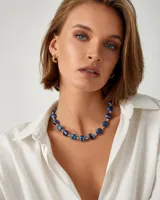 Collar corto de cuentas esféricas de acrílico en tonos azules con rayas negras y blancas, intercaladas con pequeñas cuentas metálicas.