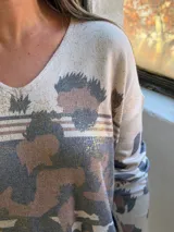 Sweater de punto con escote en V y mangas largas, de diseño holgado. Presenta un estampado animal print abstracto en tonos chocolate y detalles metalizados en color dorado sobre una base color crema.