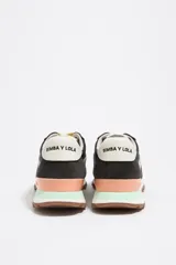 Zapatillas urbanas de la marca Bimba y Lola, confeccionadas en una combinación de serraje vacuno y tejidos técnicos. Presentan un diseño multicolor con base negra y gris, detalles en verde menta y salmón, cordones amarillos y suela dentada de caucho. Incluyen el logotipo de la marca en el estabilizador del talón y la lengüeta.