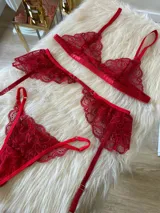 Conjunto de lencería de tres piezas en encaje rojo, compuesto por un bralette triangular, una tanga regulable y un portaligas con volados en las caderas.