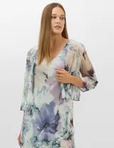 Conjunto compuesto por un vestido midi de gasa con estampado floral en tonos violeta, azul y crema, con escote en V, tirantes anchos y ruedo asimétrico con volados. Incluye una chaqueta corta tipo torera de mangas 3/4 confeccionada en la misma tela. Posee forro interno a tono.