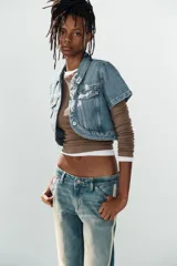 Jeans rectos de tiro medio en denim azul con efecto deslavado. Presentan bandas laterales con detalles brillantes, bolsillos delanteros y traseros, y aberturas en los tobillos con botonadura metálica.