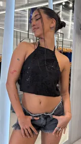 Top halter negro con escote redondo y tiras finas para anudar al cuello, confeccionado con tela transparente bordada de diseño floral y detalles de lentejuelas.