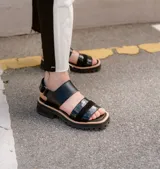 Sandalias de cuero color crudo con dos tiras horizontales en el empeine, una de cuero liso y otra con detalle dorado. Suela track color beige.