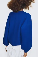 Jersey de punto color azul, con cuello redondo, mangas largas amplias y costuras marcadas en el frente.