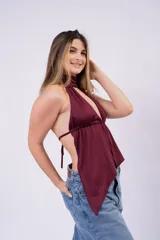 Blusa marrón con escote halter y diseño cruzado que genera un pronunciado escote en V y aberturas frontales. Confeccionada con tela ligera y drapeada, presenta un corte asimétrico con terminación en puntas colgantes.