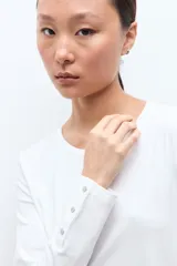 Remera de manga larga en color blanco, con cuello redondo y detalle de botones en los puños.