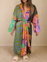 Bata tipo kimono de diseño patchwork, confeccionada con una mezcla de telas estampadas con motivos florales, paisley y geométricos en tonos verdes, naranjas y violetas. Presenta mangas tres cuartos, aberturas laterales en el ruedo y un lazo ajustable en la cintura.