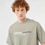 Remera de algodón verde militar, de corte holgado y manga corta, con cuello redondo y estampado frontal con texto en blanco y negro.