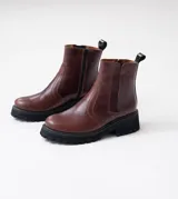 Botas Kiev de cuero vacuno color marrón, con suela de goma negra tipo track. Tienen cierre YKK en el lado interno y elástico en el lado externo. La punta es redonda y ancha.